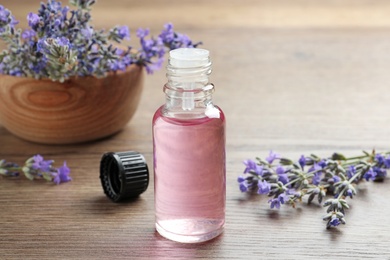 Bottle of essential oil and lavender flowers on wooden table