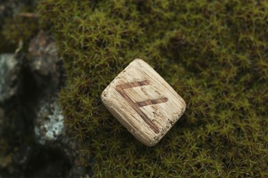 Wooden rune Ansuz on stone with moss outdoors, closeup