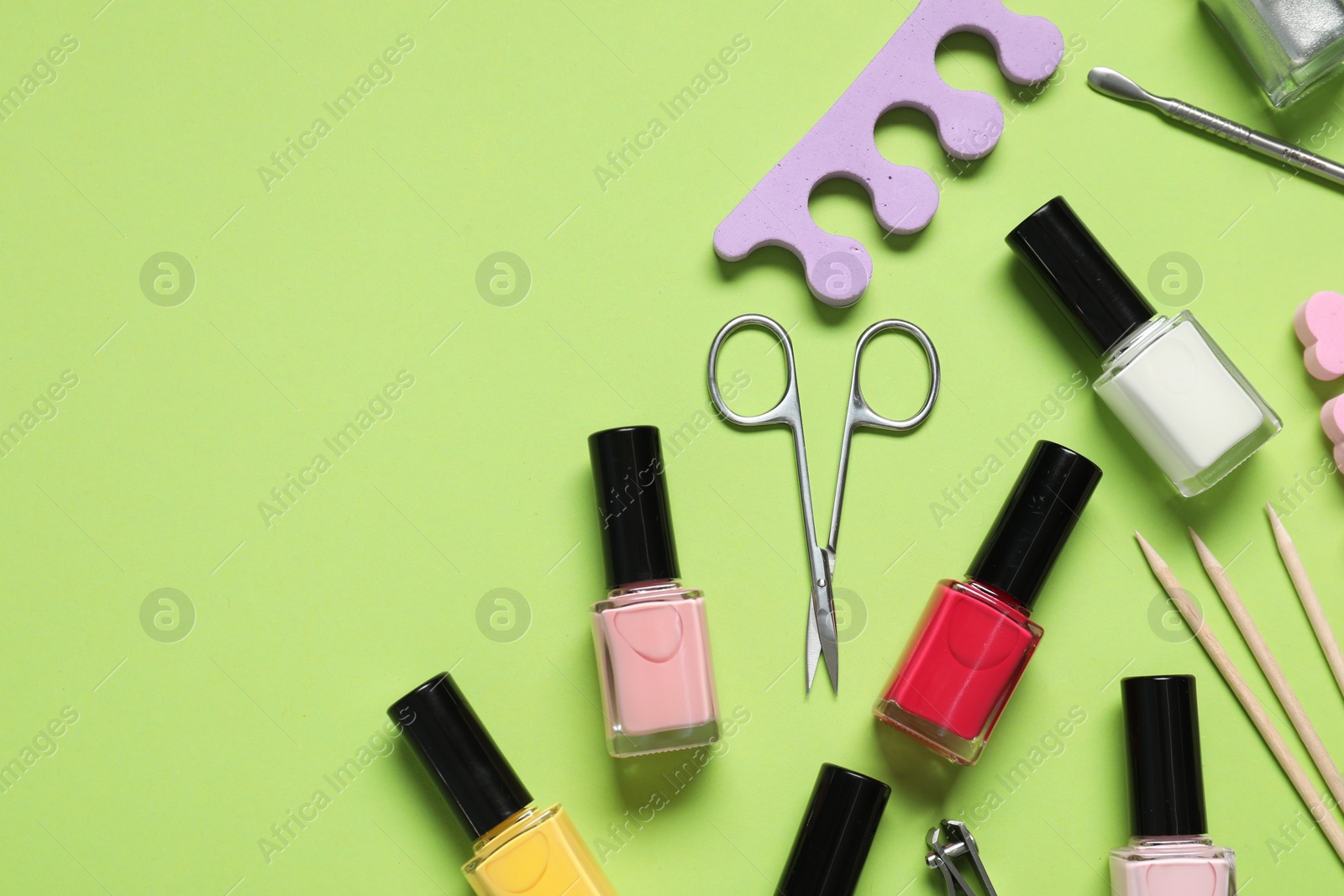 Photo of Nail polishes and set of pedicure tools on green background, flat lay. Space for text