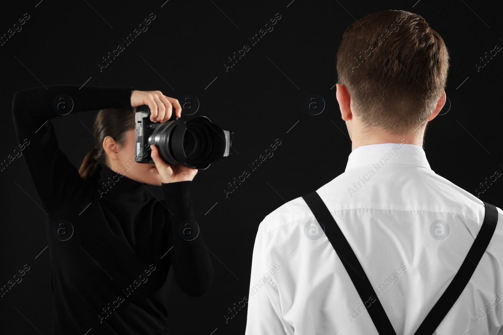 Photo of Professional photographer taking picture of man on black background, selective focus