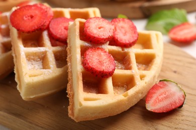 Photo of Tasty Belgian waffles with strawberries and powdered sugar on wooden board, closeup