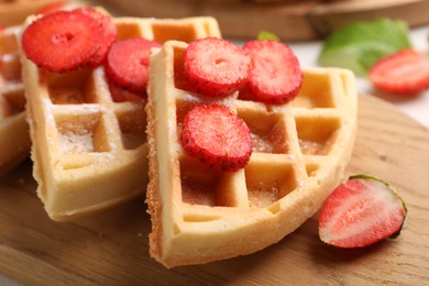 Tasty Belgian waffles with strawberries and powdered sugar on wooden board, closeup