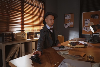 Photo of Cute little detective taking revolver at table in office