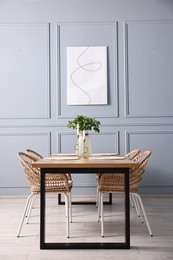 Photo of Rattan chairs, table, burning candles and vase with green branches in stylish dining room