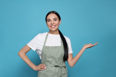 Young woman in grey apron on light blue background,