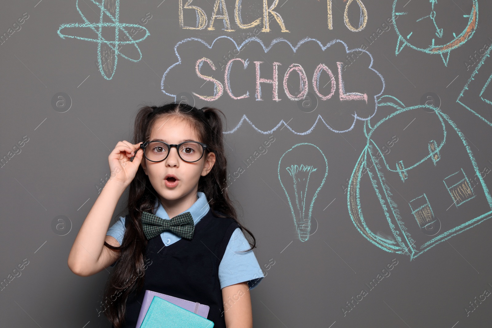 Photo of Little child in uniform near drawings with text BACK TO SCHOOL on grey background