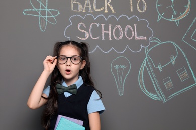 Photo of Little child in uniform near drawings with text BACK TO SCHOOL on grey background