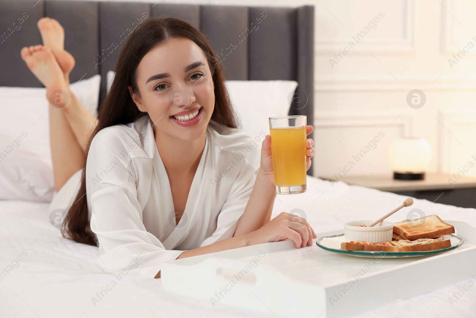 Photo of Happy young woman having breakfast on bed at home