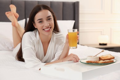 Happy young woman having breakfast on bed at home