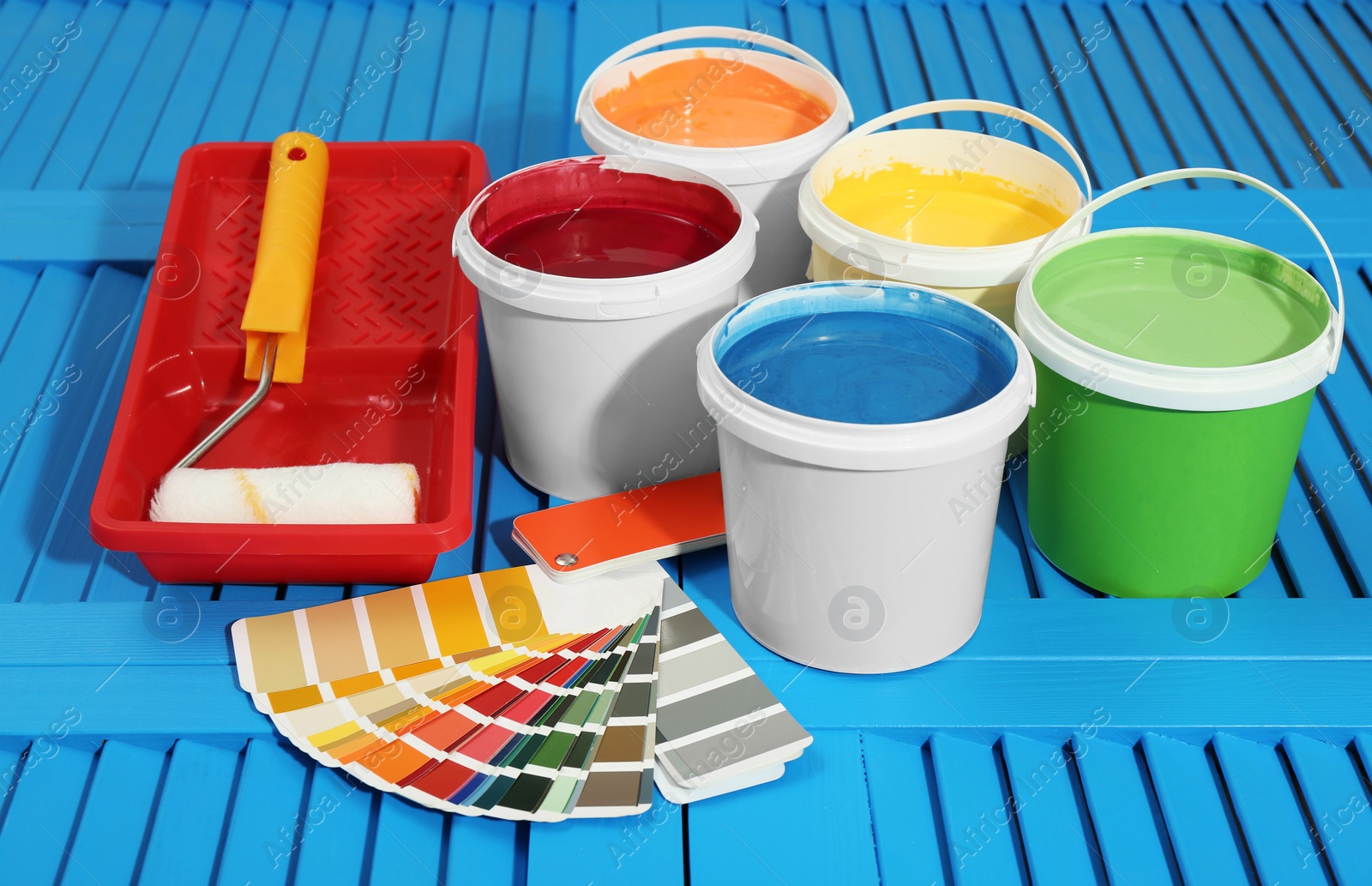 Photo of Buckets of paints, palette and decorator's tools on light blue wooden background