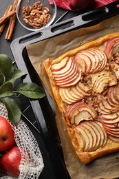 Photo of Baking tray with fresh apple galette and ingredients on black table, flat lay