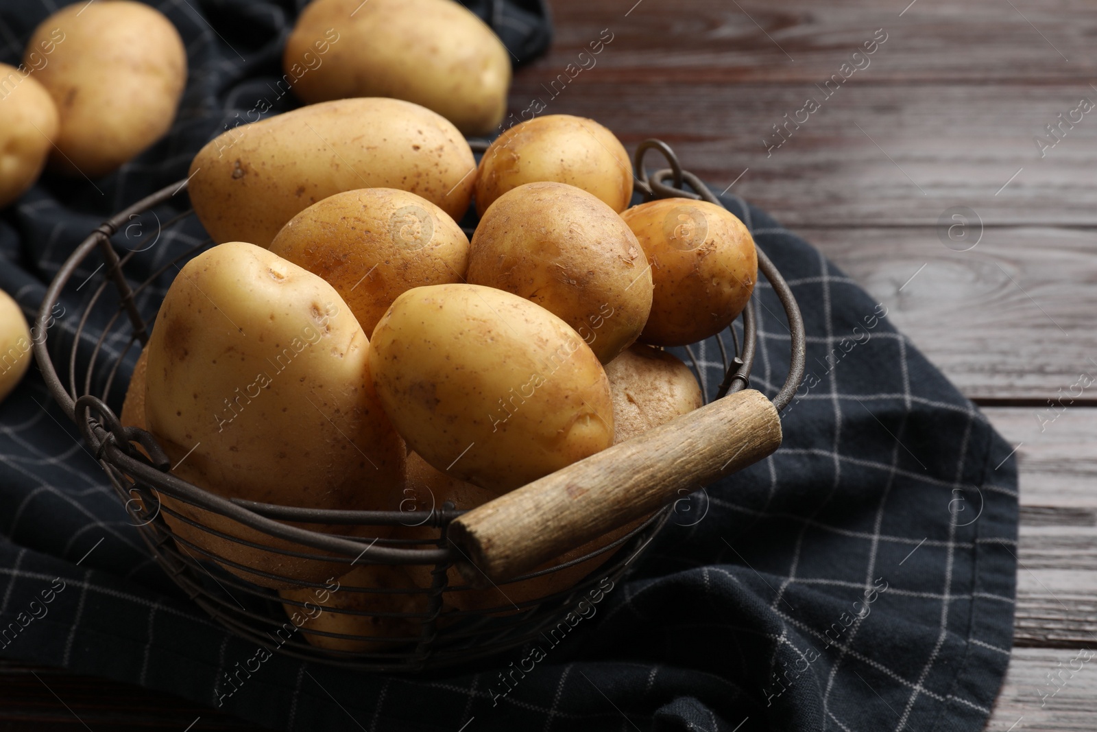 Photo of Raw fresh potatoes in metal basket on wooden table, closeup