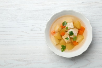 Fresh homemade chicken soup in dish on wooden background, top view with space for text