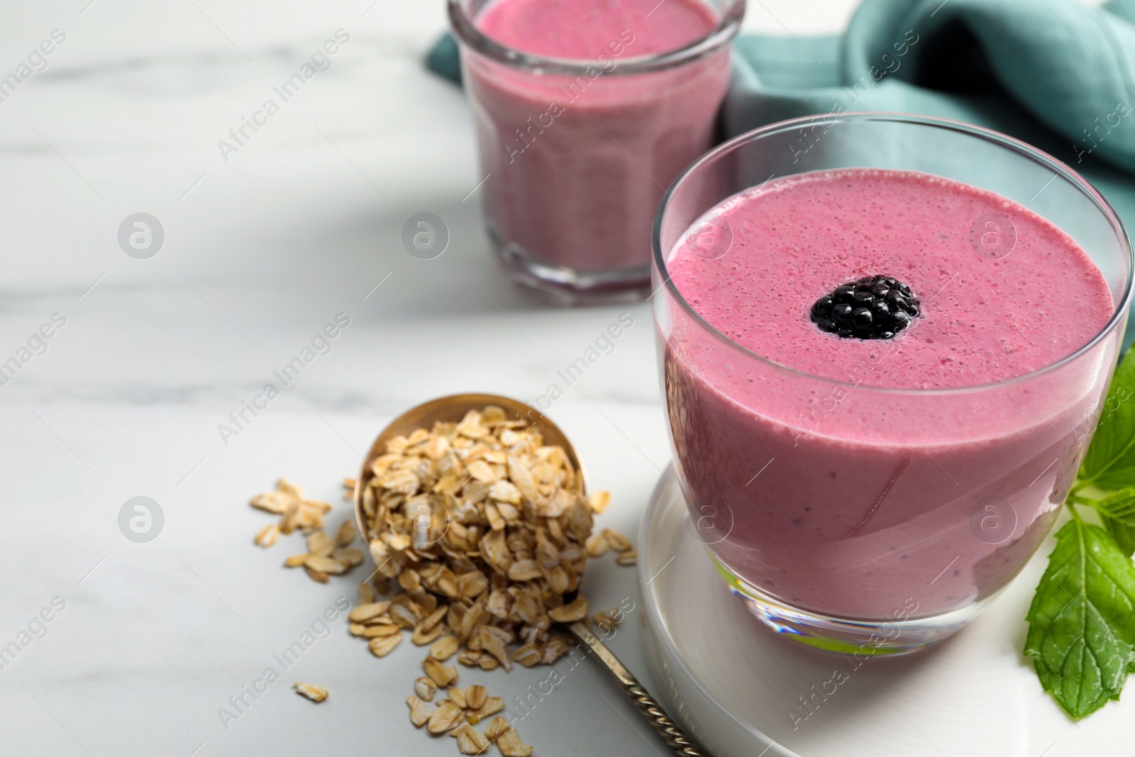 Photo of Glasses of blackberry smoothie with mint and oatmeal on white table, closeup. Space for text