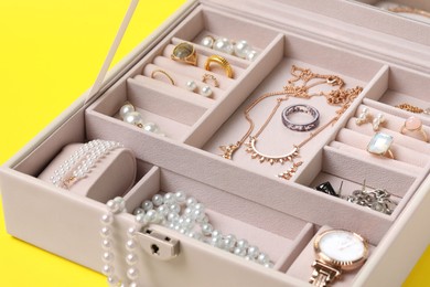 Jewelry box with many different accessories on yellow background, closeup