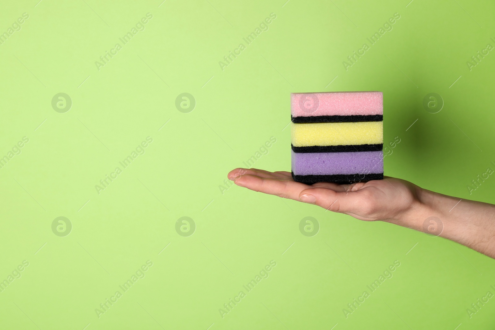 Photo of Woman holding sponges on green background, closeup. Space for text