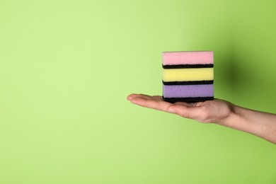 Photo of Woman holding sponges on green background, closeup. Space for text