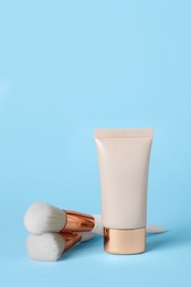 Tube of skin foundation and brushes on light blue background. Makeup product