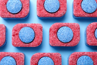 Photo of Many dishwasher detergent tablets on light blue background, flat lay