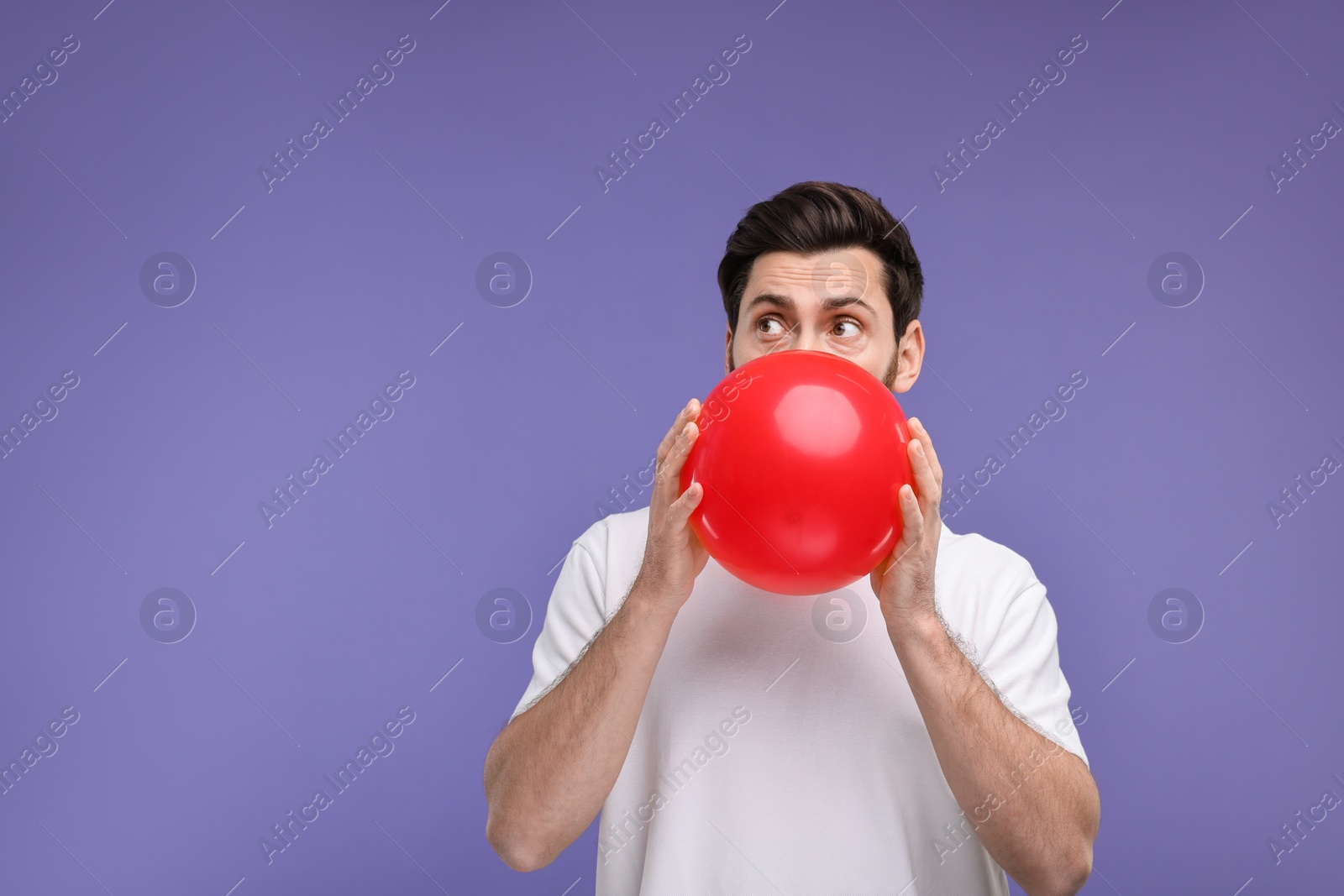 Photo of Man inflating red balloon on purple background. Space for text