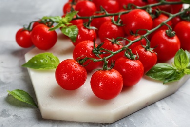 Photo of Fresh ripe cherry tomatoes with water drops and basil on table, closeup