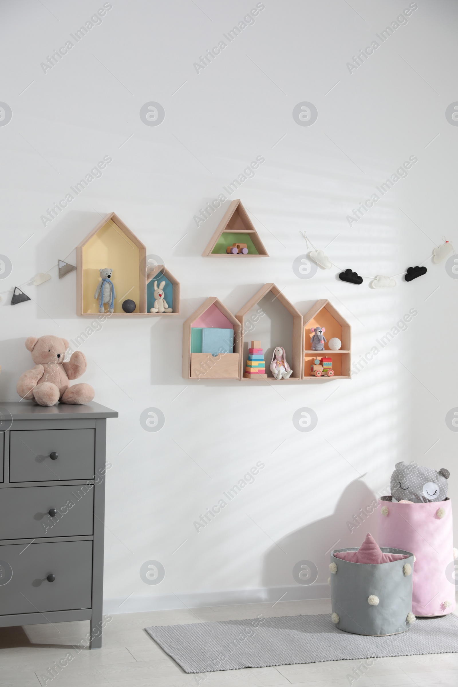 Photo of Cute children's room with house shaped shelves and chest of drawers. Interior design