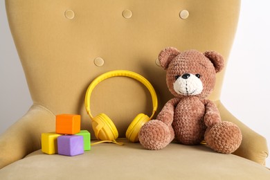Baby songs. Toy bear, headphones and cubes on armchair near white wall