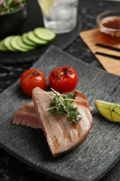 Pieces of delicious tuna with microgreens, lime and tomatoes on table, closeup