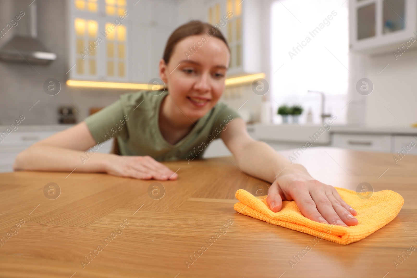 Photo of Woman with microfiber cloth cleaning wooden table in kitchen, selective focus
