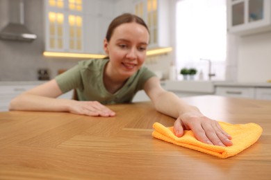 Woman with microfiber cloth cleaning wooden table in kitchen, selective focus