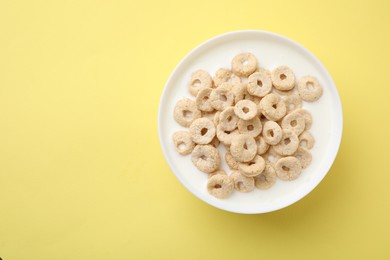 Photo of Breakfast cereal. Tasty corn rings with milk in bowl on yellow background, top view and space for text