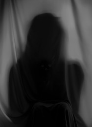 Silhouette of creepy ghost behind grey cloth