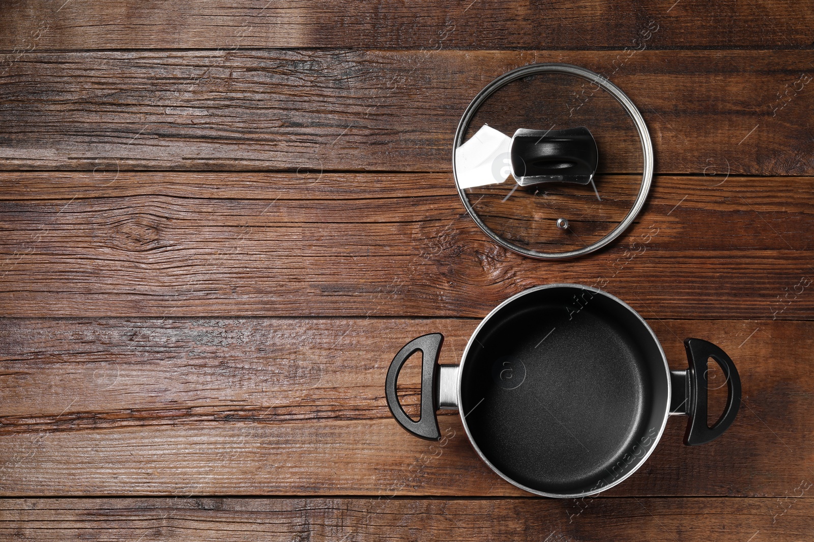 Photo of Empty black pot and glass lid on wooden table, flat lay. Space for text