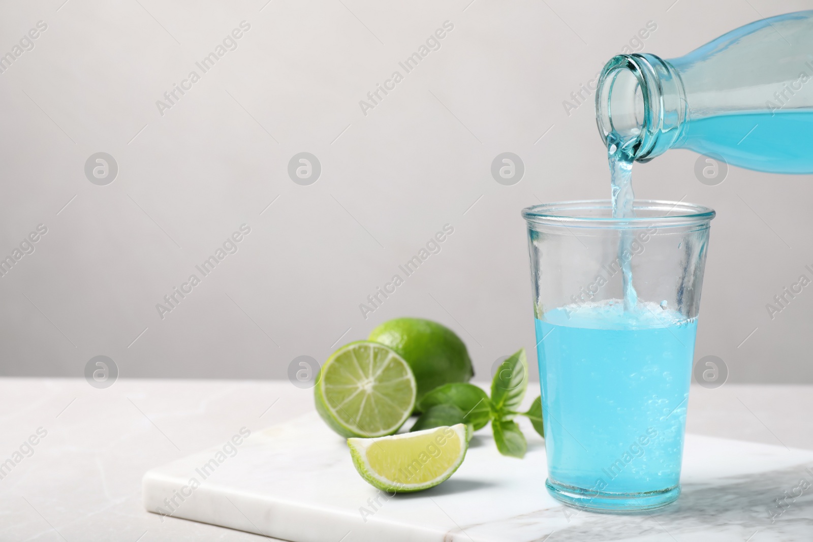 Photo of Pouring refreshing light blue drink into glass on white table, space for text