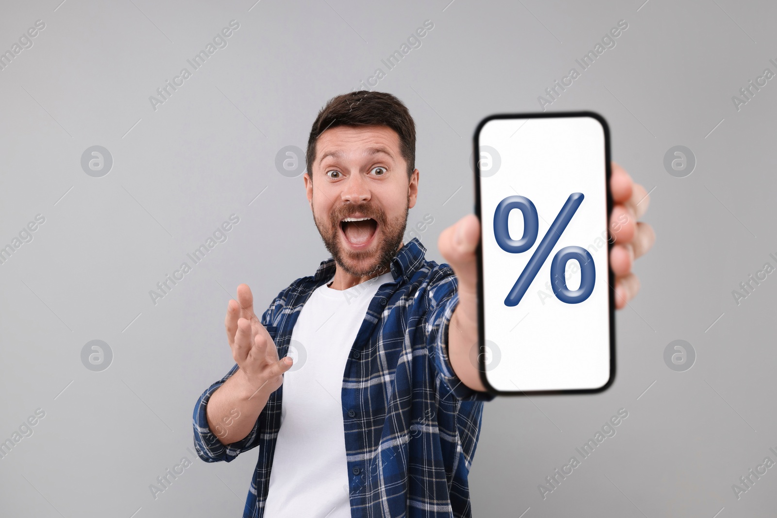 Image of Discount, offer, sale. Emotional man showing mobile phone with percent sign on screen, grey background