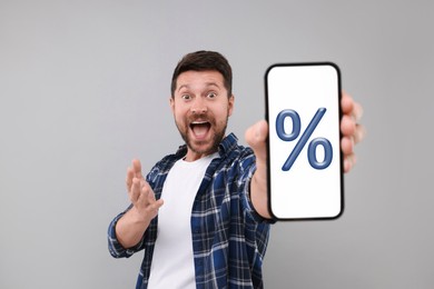 Image of Discount, offer, sale. Emotional man showing mobile phone with percent sign on screen, grey background