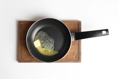 Frying pan with melting butter on board against white background, top view