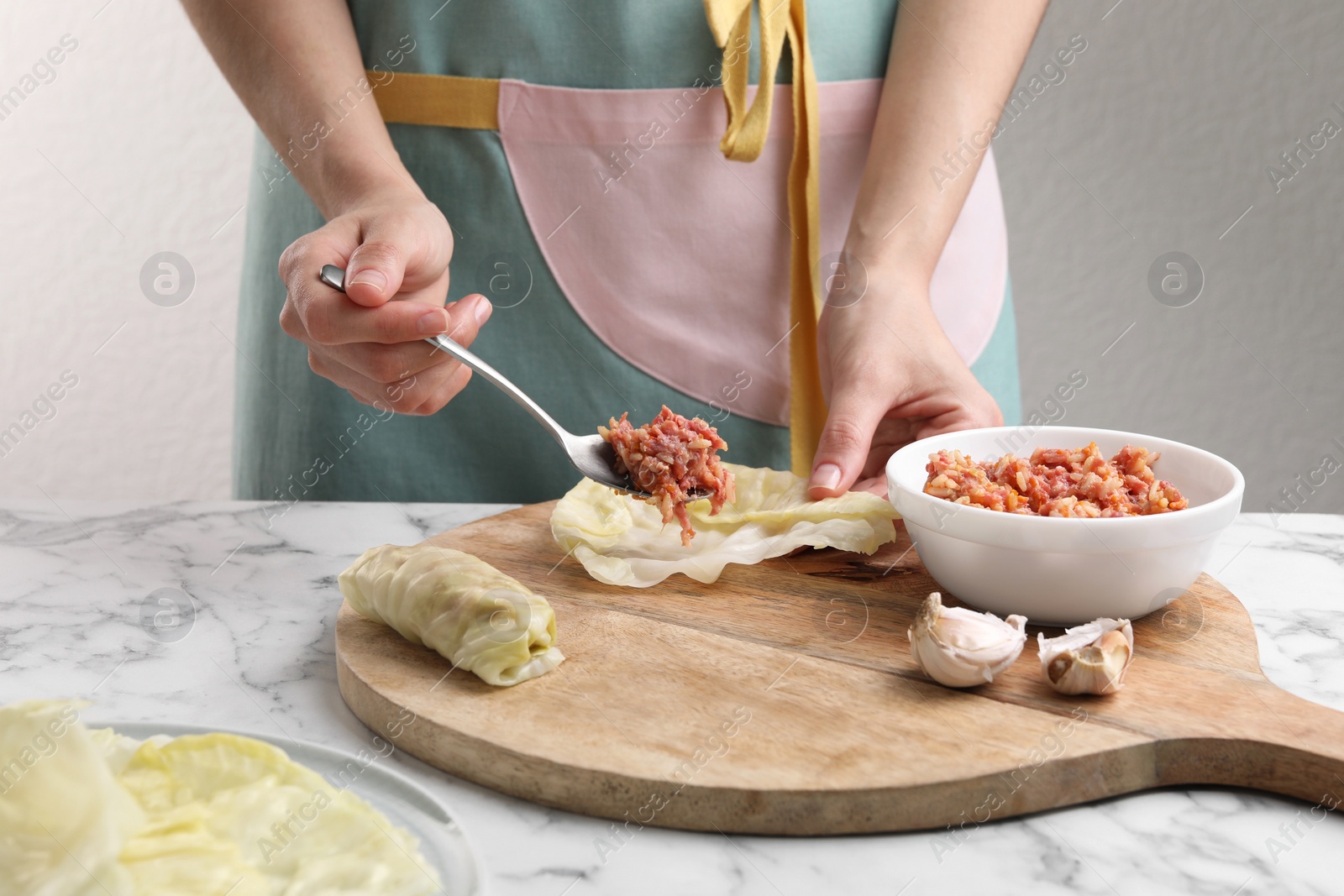 Photo of Woman preparing stuffed cabbage roll at white marble table, closeup