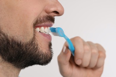 Man brushing his teeth with plastic toothbrush on white background, closeup