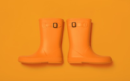 Image of Pair of bright rubber boots on orange background, top view