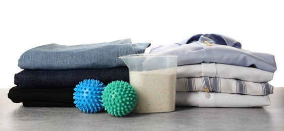 Color dryer balls, detergent and stacked clean clothes on white background