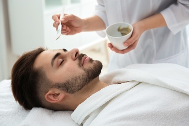 Cosmetologist applying mask on client's face in spa salon