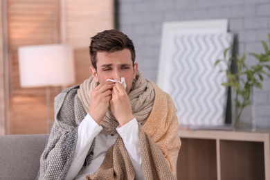 Photo of Sick young man with tissue suffering from cold at home