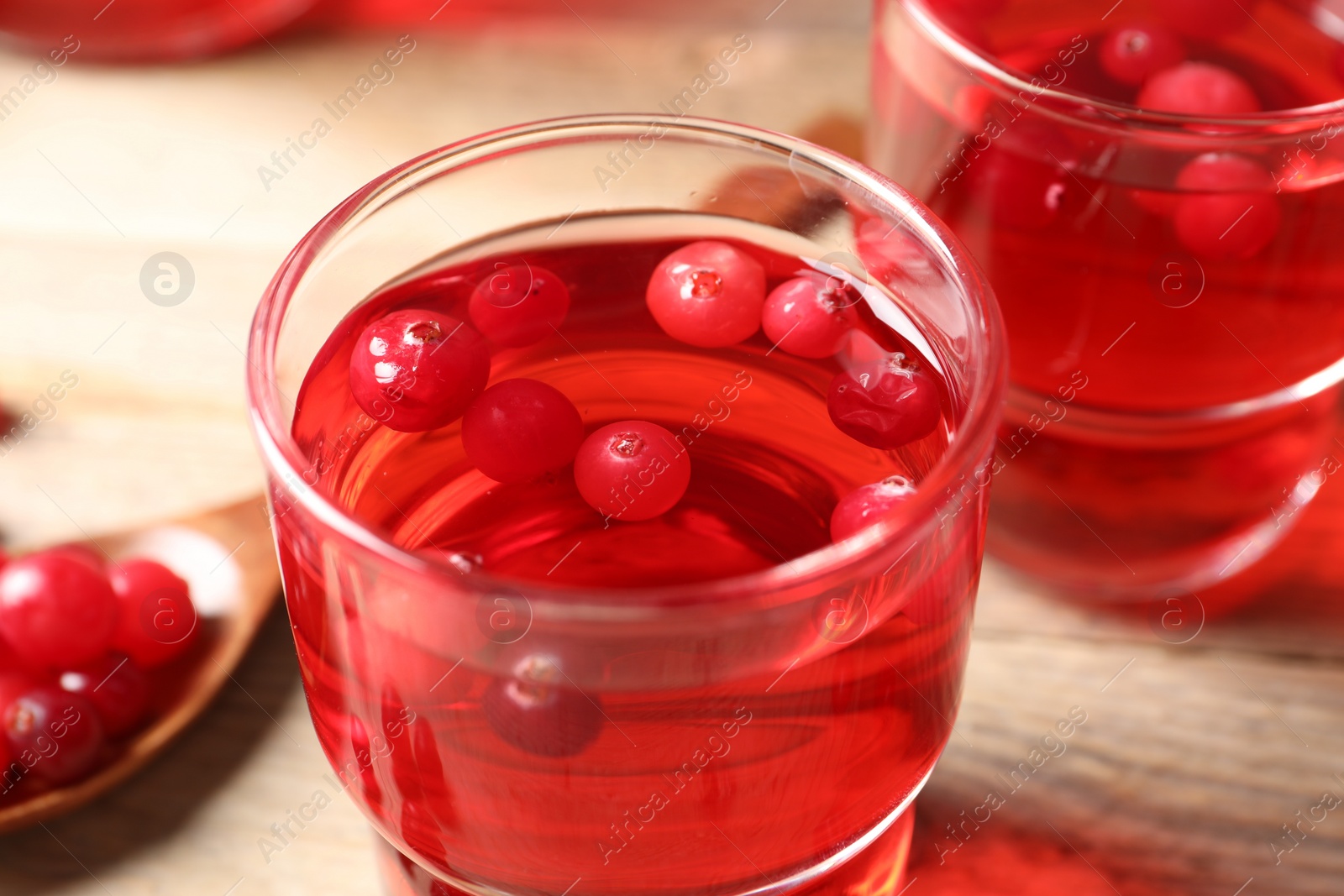 Photo of Tasty cranberry juice in glasses and fresh berries on wooden table, closeup