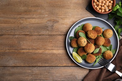 Photo of Delicious falafel balls with lime on wooden table, flat lay. Space for text