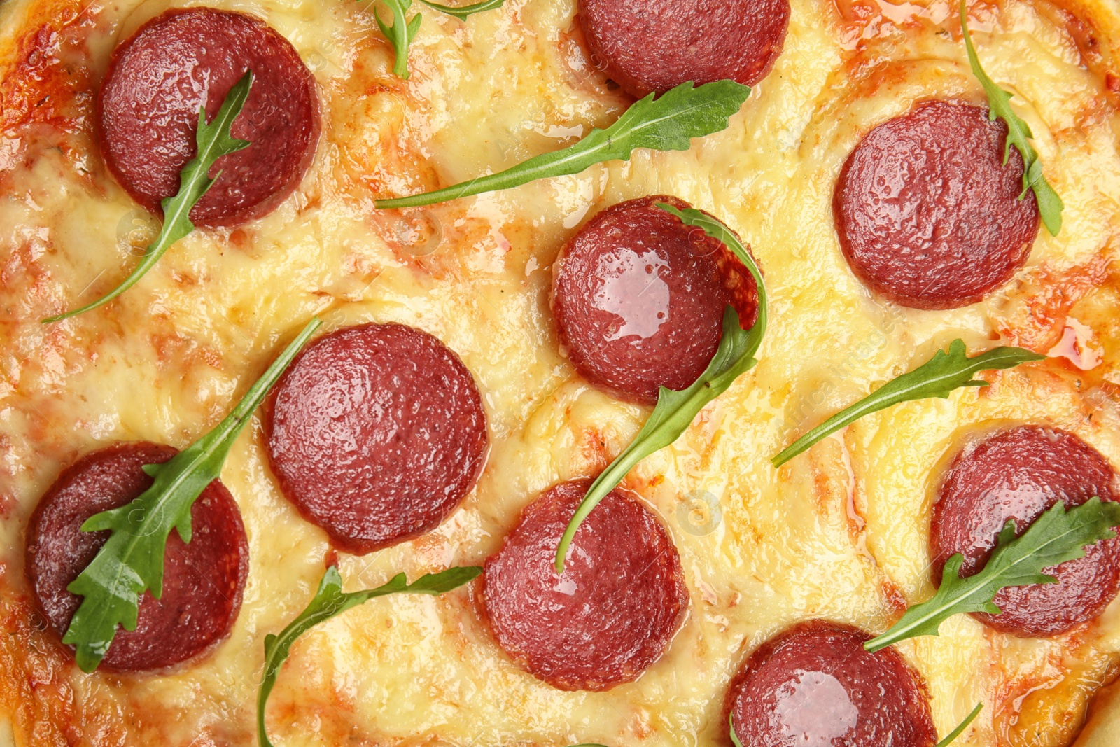 Photo of Tasty pepperoni pizza with arugula as background, top view