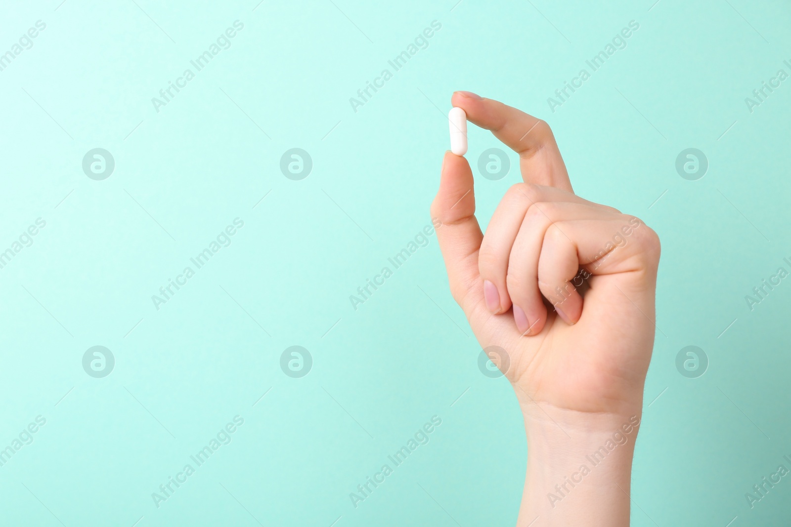 Photo of Woman holding vitamin capsule on turquoise background, closeup. Space for text