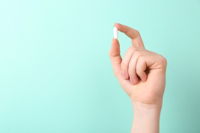 Woman holding vitamin capsule on turquoise background, closeup. Space for text