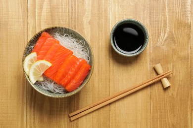 Photo of Delicious salmon sashimi served with funchosa, lemon and soy sauce on wooden table, flat lay