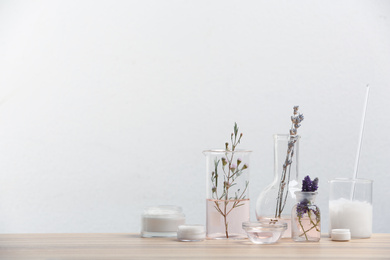 Photo of Herbal cosmetic products, laboratory glassware and ingredients on wooden table. Space for text